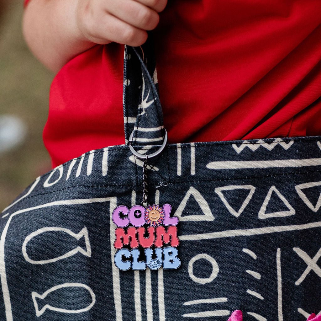 A black metal keyring with the text 'COOL MUM CLUB' in colorful letters attached to a bag.