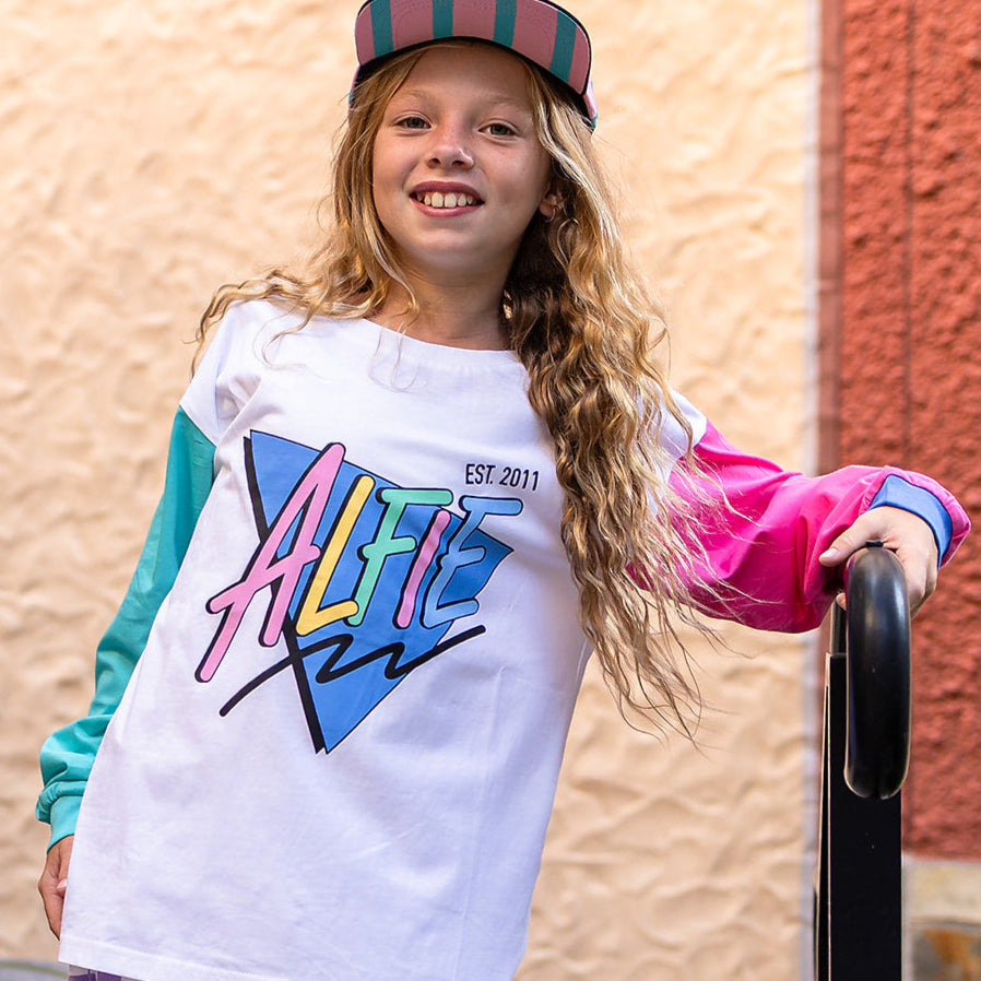 A child wearing a long sleeve white t-shirt with colorful stripes and the brand name 'Alfie' displayed prominently on the front.