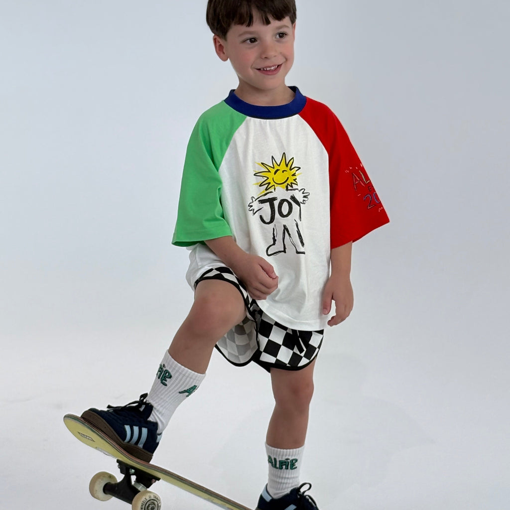 Child wearing a colorful shirt and checkered shorts, sitting on a skateboard against a white background